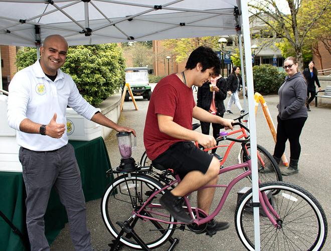 在不列颠哥伦比亚省校园的一个帐篷里，一名学生骑着自行车演示如何调制饮料.