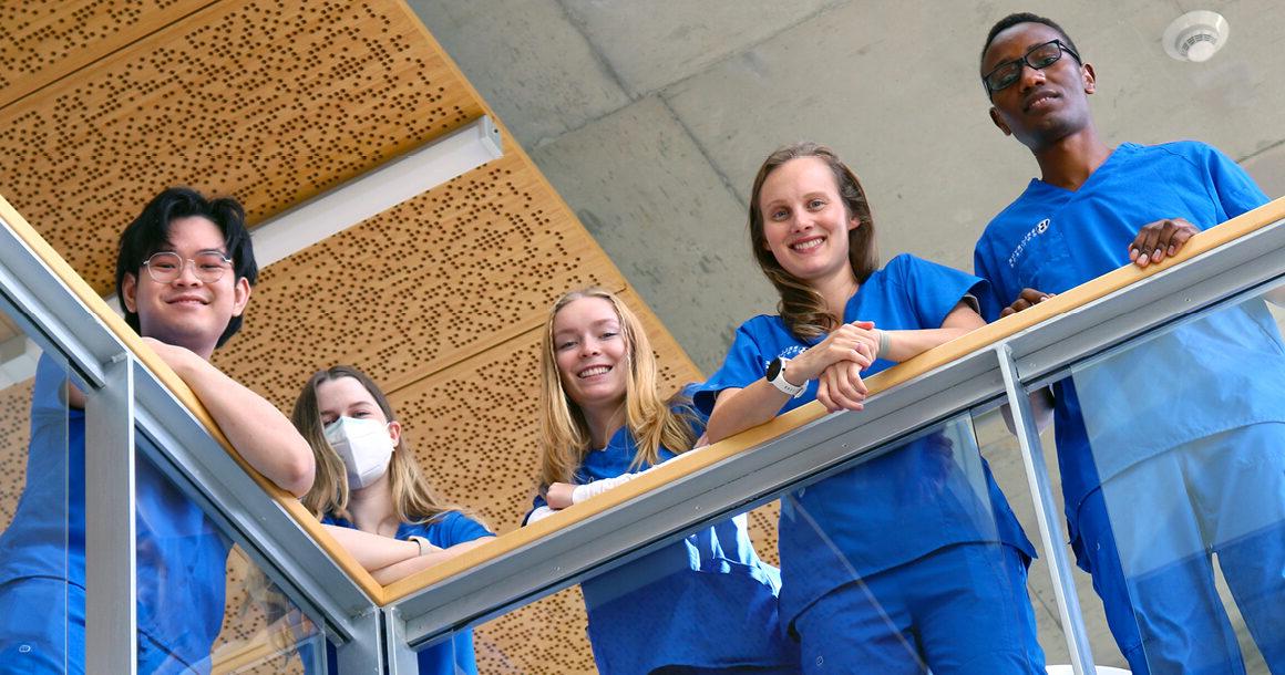 Students in scrubs lean over a campus balcony.